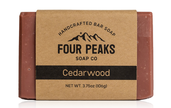 A bar of handcrafted soap from Four Peaks Soap Co. labeled "Cedarwood." The soap is wrapped in a brown paper band with a mountain logo and text indicating it weighs 3.75 ounces (106 grams).