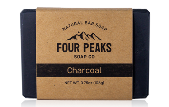A bar of handcrafted soap from Four Peaks Soap Co. labeled "Charcoal." The soap is wrapped in a brown paper band with a mountain logo and text indicating it weighs 3.75 ounces (106 grams).