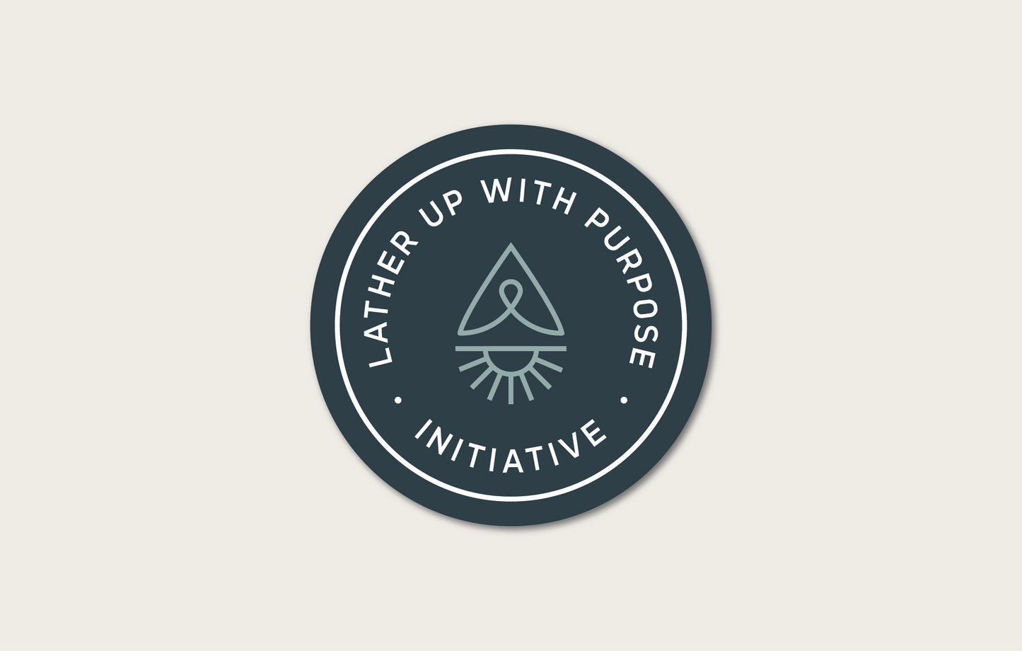 A sticker of the "Lather Up With Purpose" Initiative. The logo features a circular shape with text that reads "Lather Up With Purpose Initiative". Inside the circle there is an icon of sun, cancer ribbon, and compass arrow that when combined represents a water drop. The logo has a blue and teal color scheme.