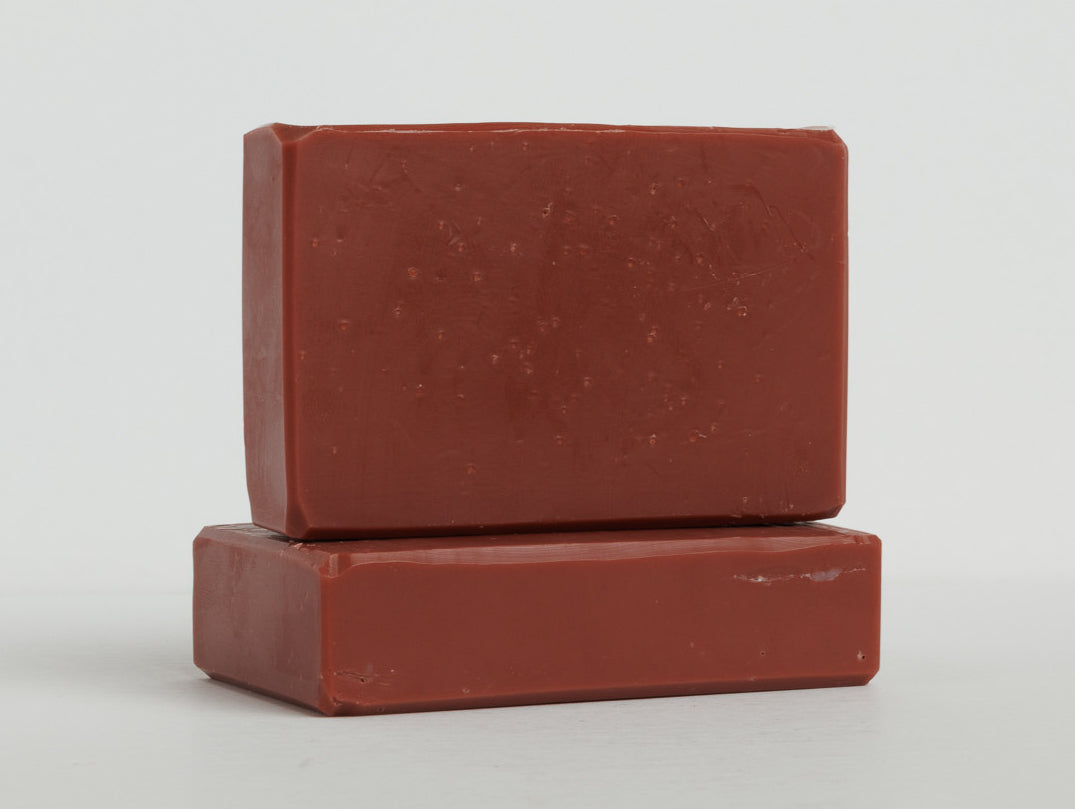 Two maroon bars of soap are stacked on a clean white surface with one bar lying flat and the other placed upright on top. The soaps have a smooth texture and rectangular shape with slightly rounded edges.