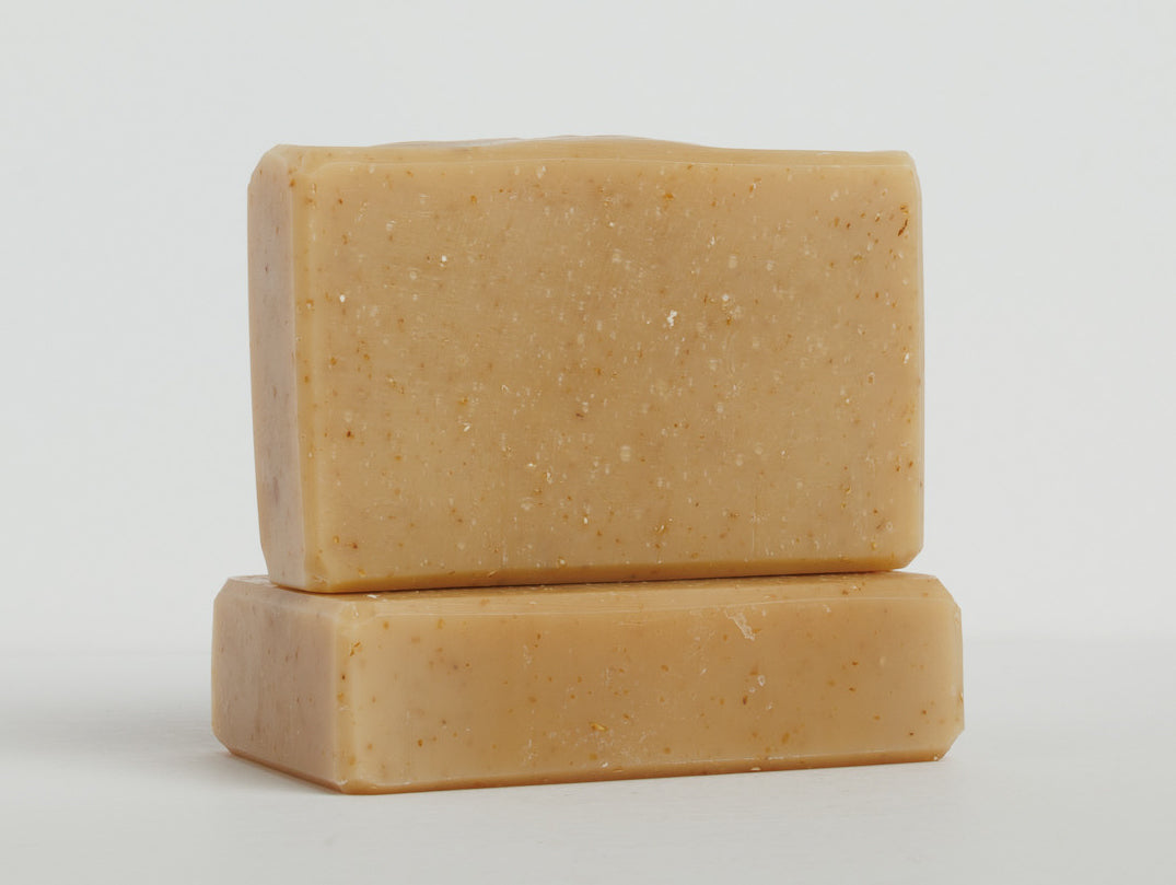 Two beige bars of soap are stacked on a clean white surface with one bar lying flat and the other placed upright on top. The soaps have a smooth texture and rectangular shape with slightly rounded edges.