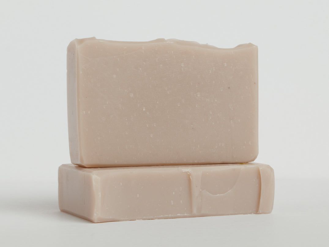Two mauve bars of soap are stacked on a clean white surface with one bar lying flat and the other placed upright on top. The soaps have a smooth texture and rectangular shape with slightly rounded edges.