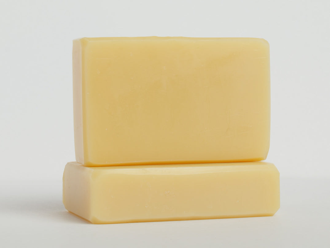 Two yellow bars of soap are stacked on a clean white surface with one bar lying flat and the other placed upright on top. The soaps have a smooth texture and rectangular shape with slightly rounded edges.