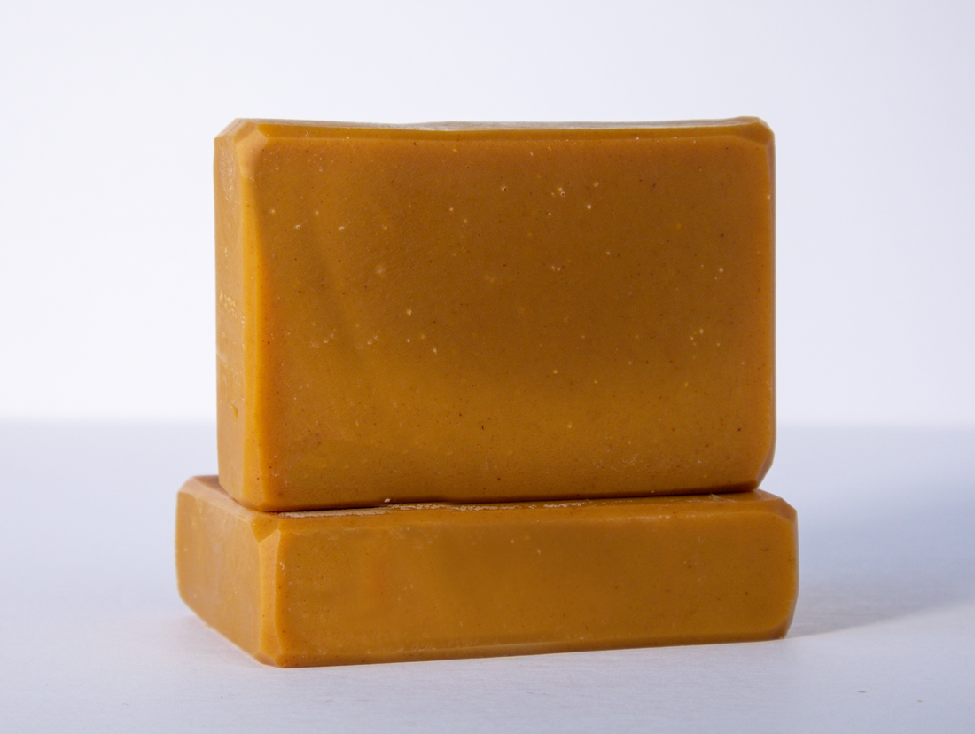 Two orange bars of soap are stacked on a clean white surface with one bar lying flat and the other placed upright on top. The soaps have a smooth texture and rectangular shape with slightly rounded edges.