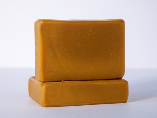Two orange bars of soap are stacked on a clean white surface with one bar lying flat and the other placed upright on top. The soaps have a smooth texture and rectangular shape with slightly rounded edges.