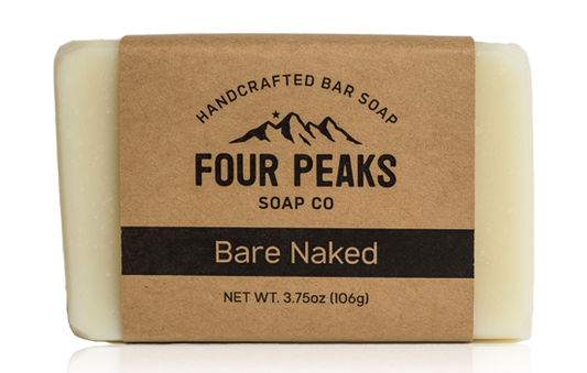 A bar of handcrafted soap from Four Peaks Soap Co. labeled "Bare Naked." The soap is wrapped in a brown paper band with a mountain logo and text indicating it weighs 3.75 ounces (106 grams).
