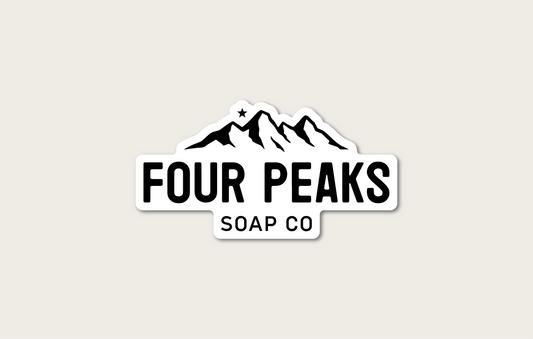 A sticker of the Four Peaks Soap Co logo. The logo features an illustration of mountain peaks with a star above them. Below the peaks, it says "Four Peaks Soap Co". The logo has a white and black color scheme.