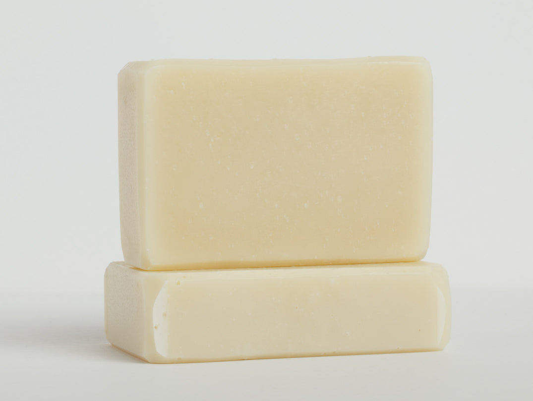Two ivory white bars of soap are stacked on a clean white surface with one bar lying flat and the other placed upright on top. The soaps have a smooth texture and rectangular shape with slightly rounded edges.